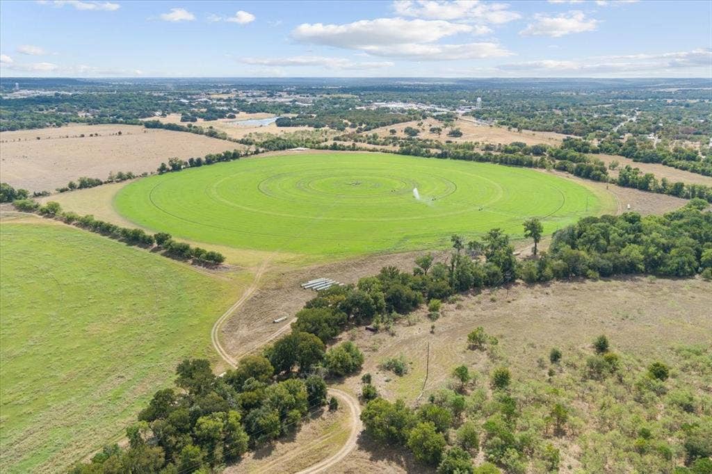 Expansive cultivated fields featuring a circular irrigation system, bordered by mature trees and natural vegetation