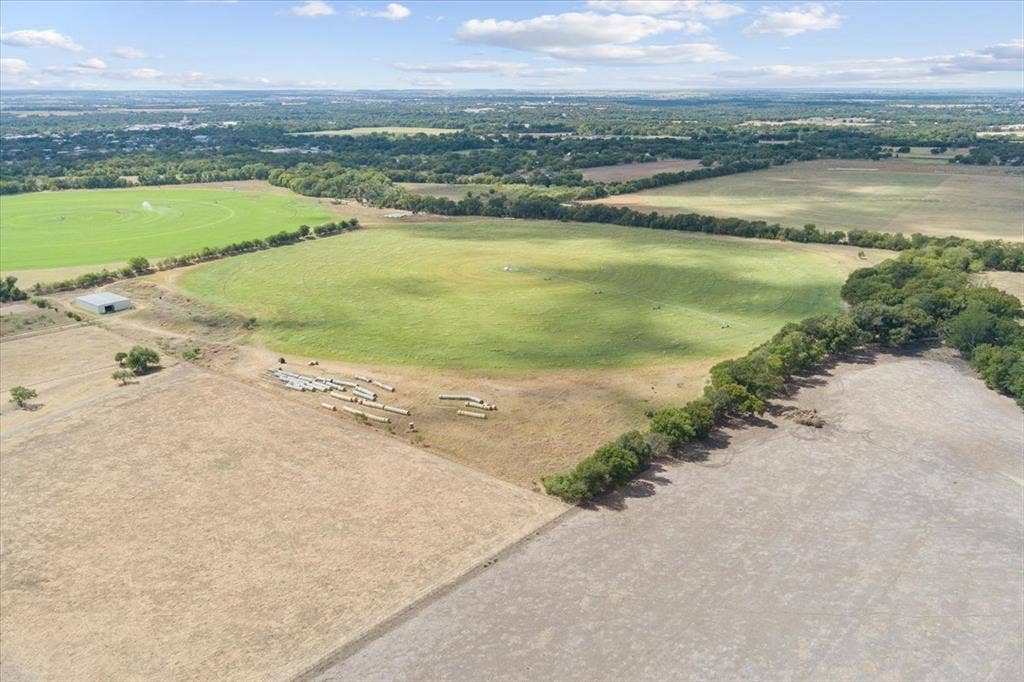 Expansive agricultural land featuring a large green field, additional cultivated fields, a metal utility building, and a distant treeline