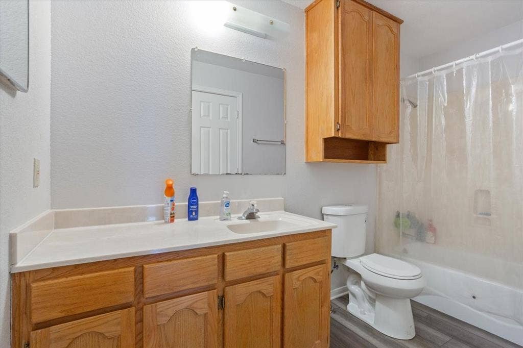 Bathroom featuring wood-finish vanity, integrated sink, wall-mounted mirror, and a full bathtub with shower