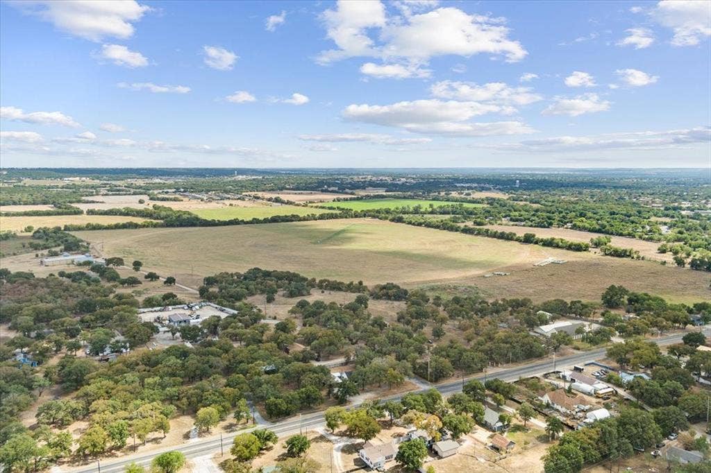 Expansive land parcel featuring open fields and mature trees, bordered by a paved road