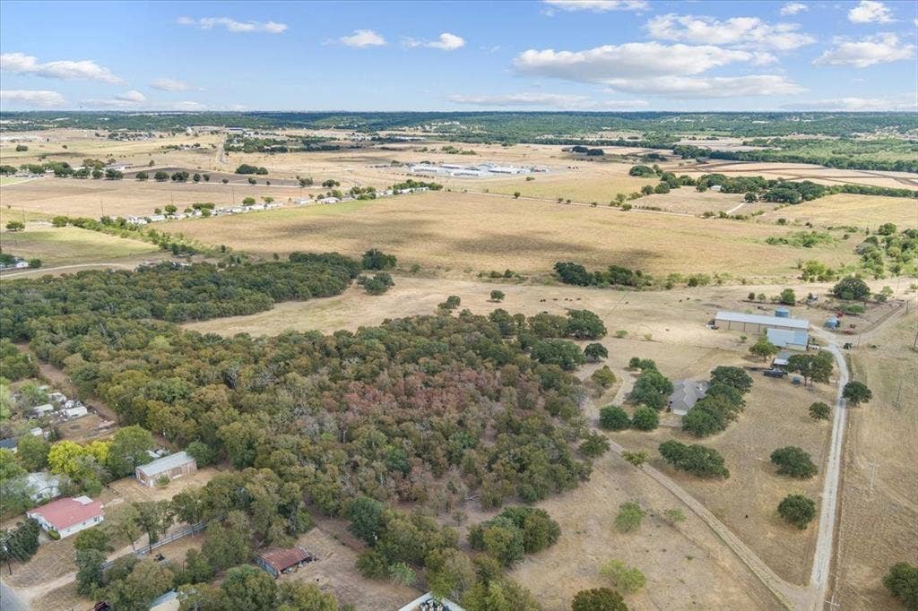 Expansive acreage featuring mixed terrain, a clustered tree line, and an outbuilding structure