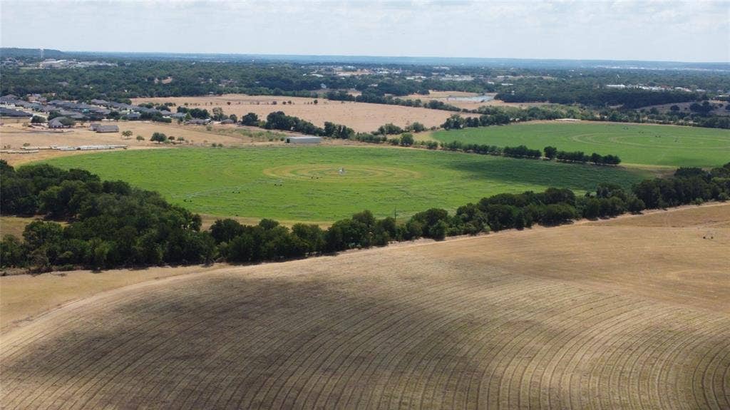 Expansive rural landscape featuring fields with varied vegetation and distant residential developments