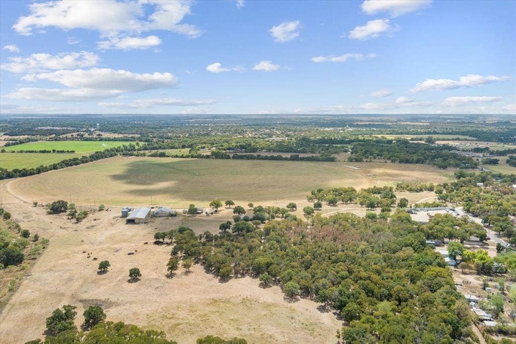 Expansive land featuring a large agricultural field, multiple structures including a barn, and scattered mature trees