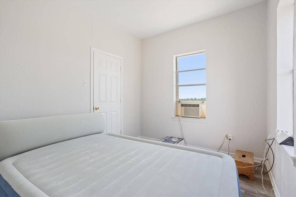 White painted interior walls, rectangular window with gridded panes, interior door with gold-finish hardware, and wood-finish flooring