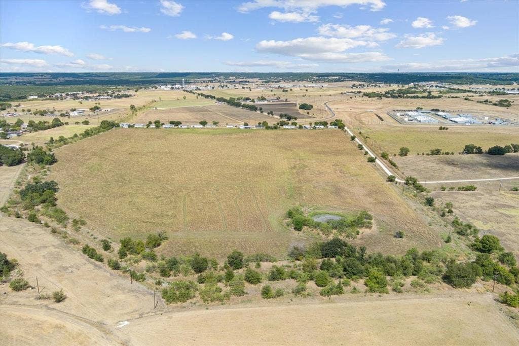 Expansive open land with a visible pond, surrounded by varied terrain and distant development