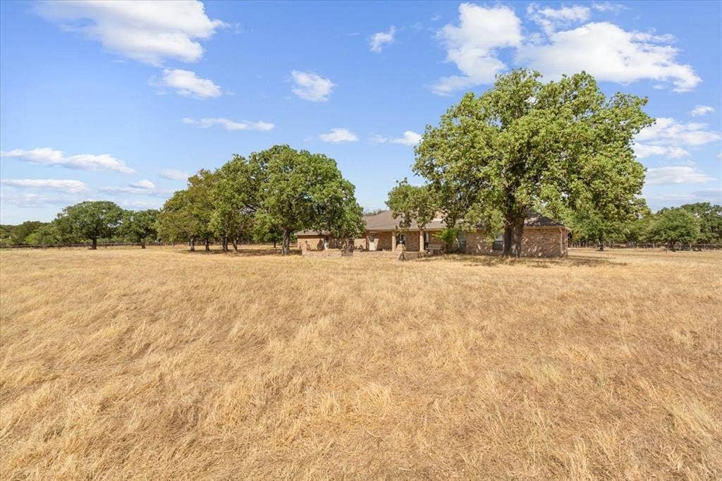 Expansive golden field with mature trees and a stone exterior residence