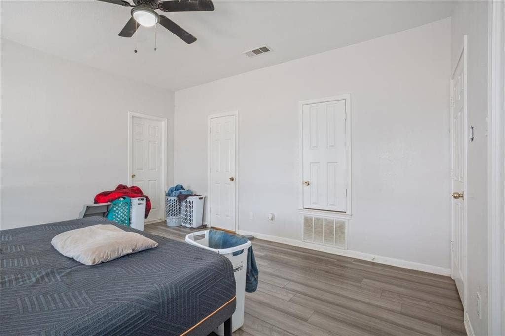 Wood-finish flooring with white baseboards, a ceiling fan with integrated lighting, and multiple panel doors