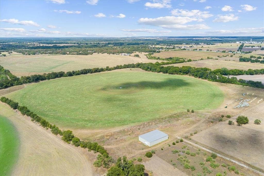Expansive green acreage featuring a circular field, scattered trees, and a metal utility building