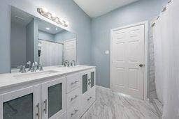 12770 E US 175 E, Larue, TX 75770 Bathroom featuring a dual-sink vanity with white cabinetry, stone-finish countertops, wall-to-wall vanity mirror, and light-tone flooring with veining