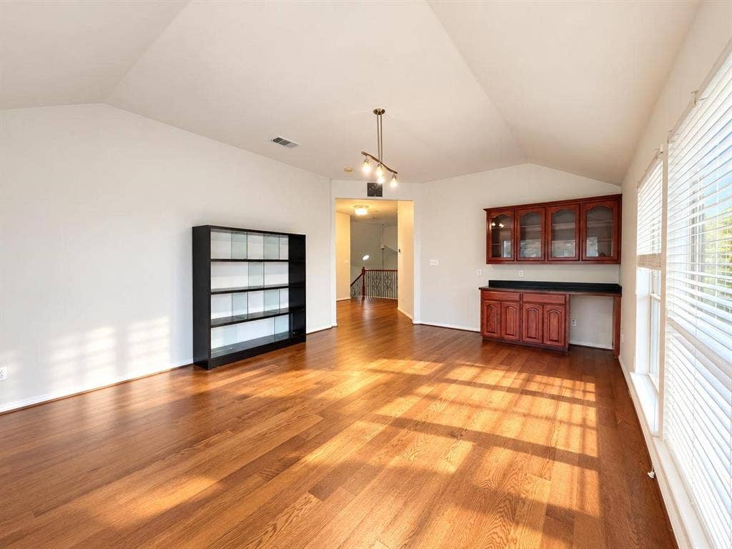 2917 Waterford Drive, Irving, TX 75063 Vaulted ceiling, wood-finish flooring, track lighting, built-in cabinetry with glass-front uppers, and large windows with blinds