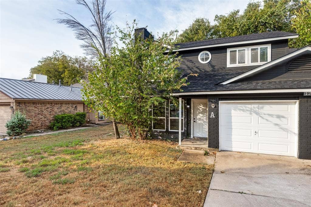 12206 Tyson Cove, #A, Austin, TX 78758 Two-story exterior with dark siding and brick accents, featuring a white garage door and a round window on the upper level
