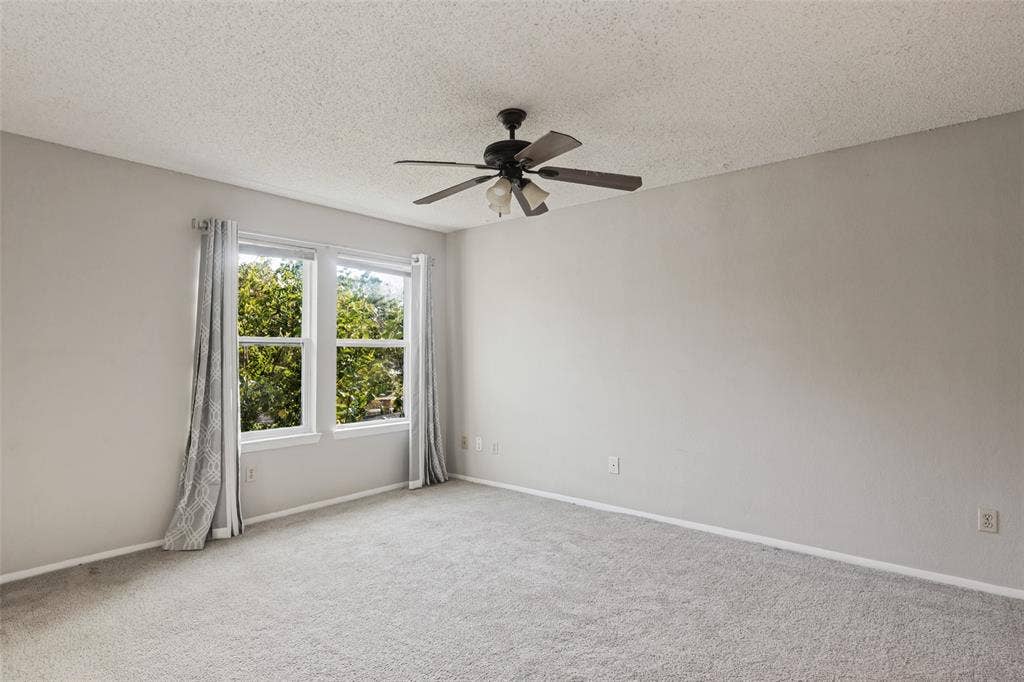 12206 Tyson Cove, #A, Austin, TX 78758 Plush gray carpeting throughout, featuring two windows with white framing and a ceiling fan with integrated lighting