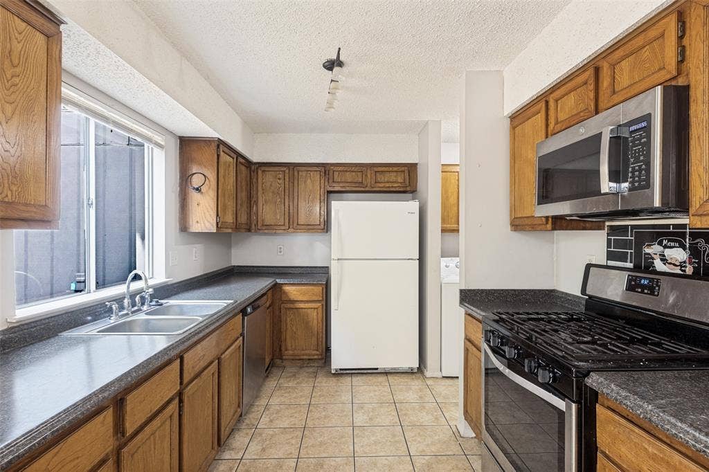 12206 Tyson Cove, #A, Austin, TX 78758 Kitchen featuring wood cabinetry, stainless steel microwave, gas range, double basin stainless steel sink, and tile flooring
