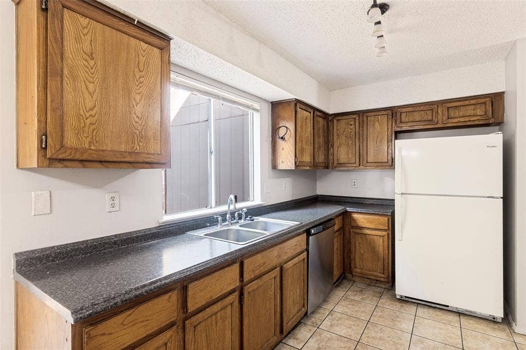 12206 Tyson Cove, #A, Austin, TX 78758 Galley kitchen featuring wood-finish cabinetry, dark stone countertops, stainless steel appliances including a gas range, and a white refrigerator