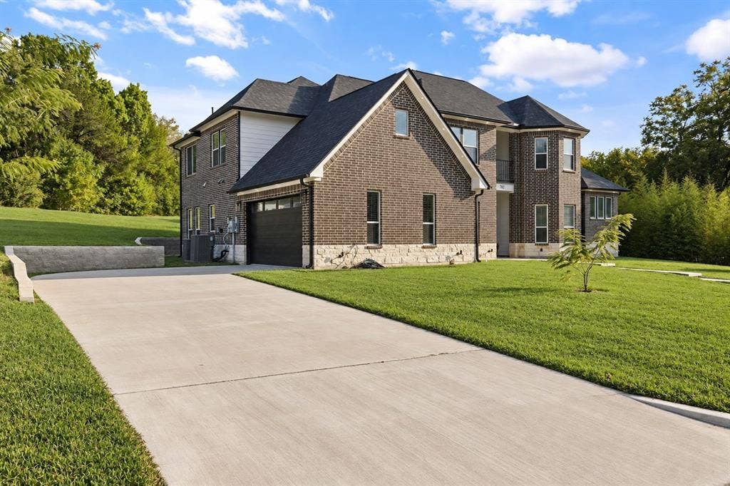 702 Linkcrest Drive, Duncanville, TX 75137 Brick exterior with stone accents, dark-paneled garage door, concrete driveway, lush green lawn, and mature trees