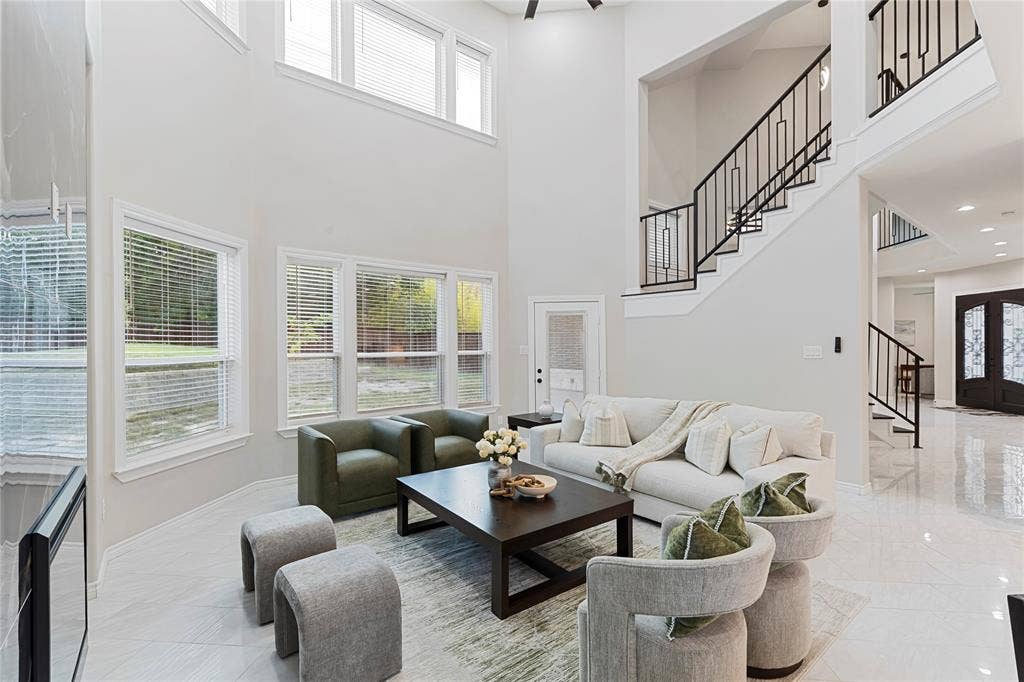 702 Linkcrest Drive, Duncanville, TX 75137 Two-story living area featuring a prominent staircase with black wrought iron balusters, multiple large windows, and high ceilings