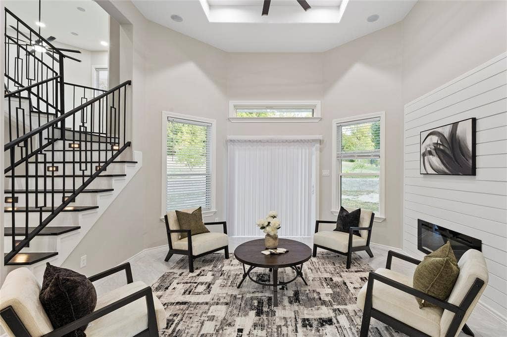 702 Linkcrest Drive, Duncanville, TX 75137 Vaulted ceiling with integrated lighting, contemporary black metal staircase with under-stair illumination, multiple windows with blinds, shiplap accent wall, and a built-in linear fireplace