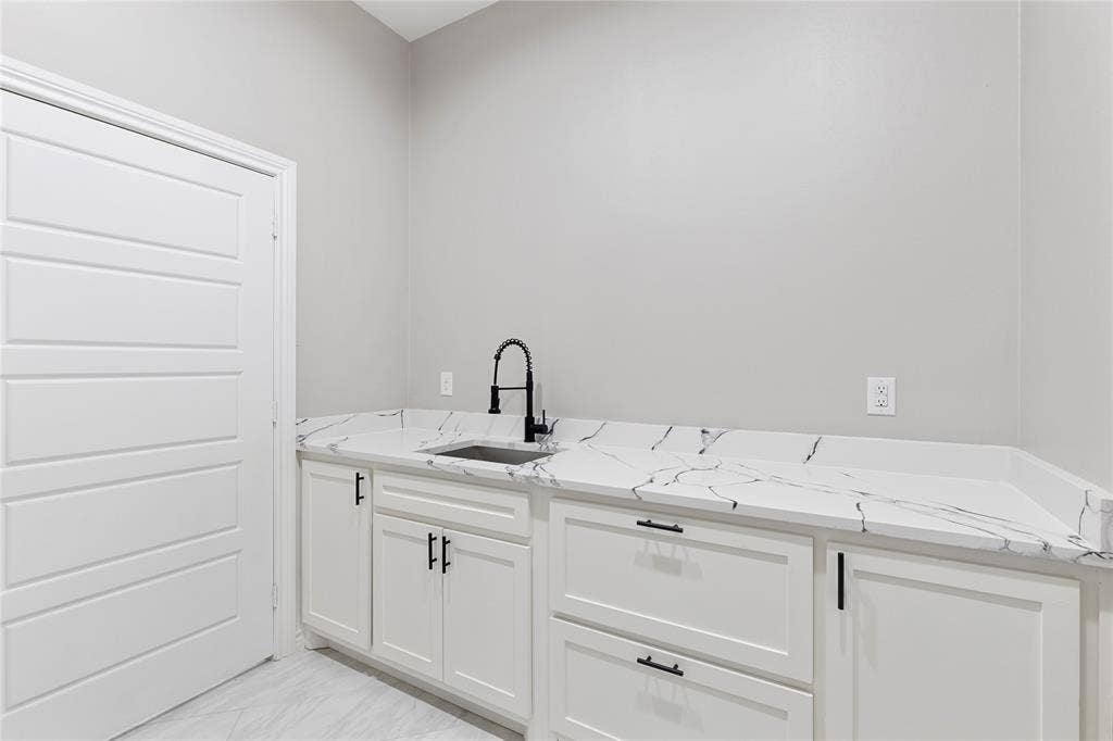 702 Linkcrest Drive, Duncanville, TX 75137 White cabinetry with matte black hardware, integrated sink, and patterned stone-finish countertop