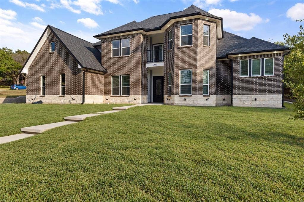 702 Linkcrest Drive, Duncanville, TX 75137 Two-story brick exterior with stone accents, multiple windows, a second-story balcony, and a prominent front entrance