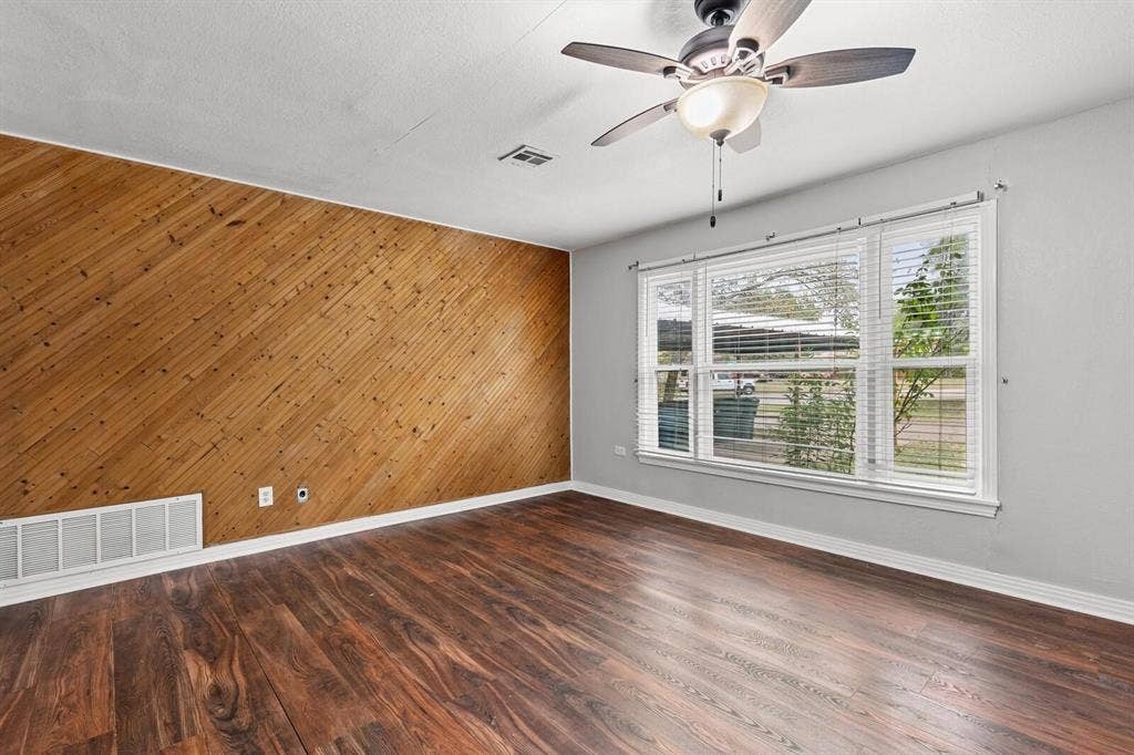 4205 Fort Avenue, Waco, TX 76710 Wood-finish flooring, accent wall with diagonal wood paneling, multi-panel windows with blinds, and a ceiling fan with integrated lighting