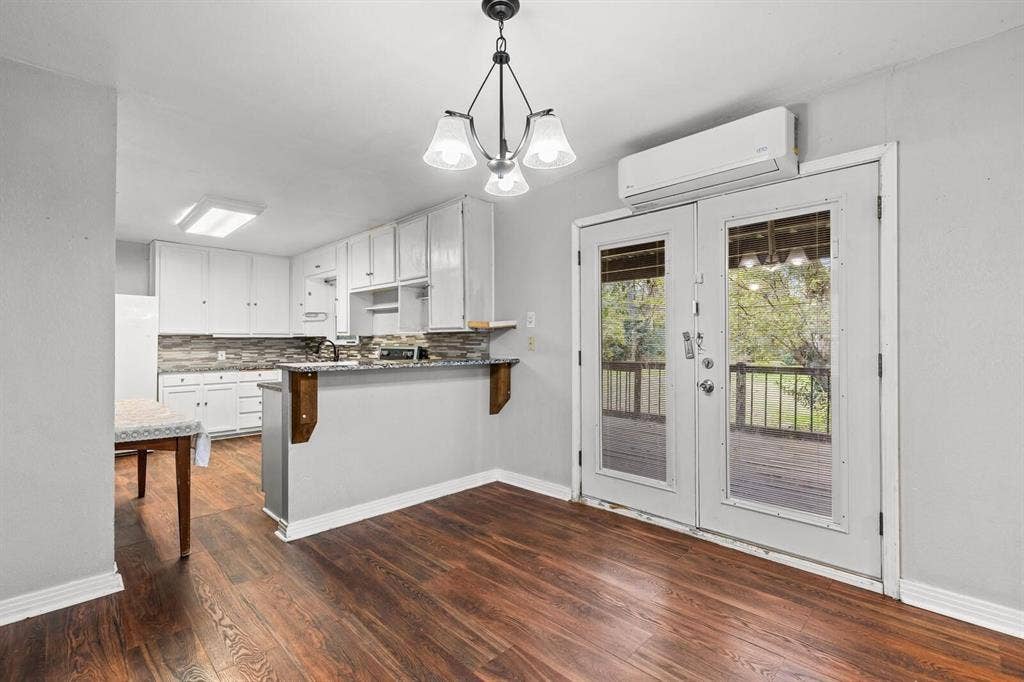 4205 Fort Avenue, Waco, TX 76710 Wood-finish flooring throughout, white kitchen cabinetry with a mosaic tile backsplash, solid surface countertops, and white French doors opening to an outdoor deck