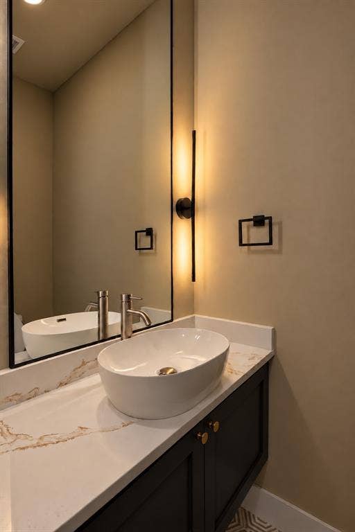 314 Avenue L, Dallas, TX 75203 Vessel sink with a brushed nickel faucet, set on a white countertop with brown veining, above a dark vanity with gold-toned cabinet pulls
