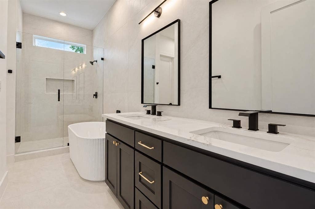 314 Avenue L, Dallas, TX 75203 Dual vanity with integrated sinks and black cabinetry, frameless shower with glass enclosure, freestanding fluted bathtub, transom window, and tiled walls
