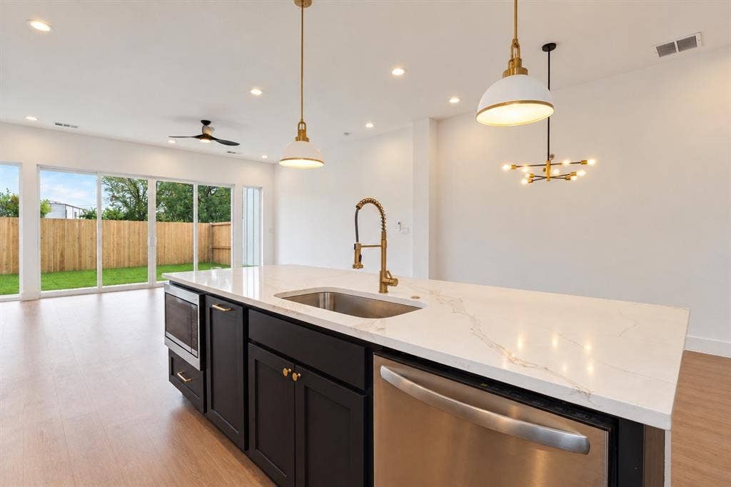 314 Avenue L, Dallas, TX 75203 Kitchen island with a white countertop and integrated sink, stainless steel dishwasher, wood-finish flooring, and pendant lighting