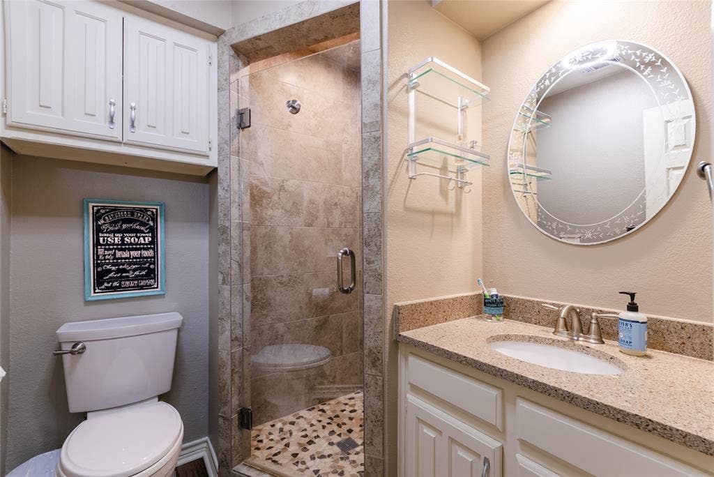 4009 Wilshire Court, Plano, TX 75023 Bathroom featuring a frameless glass shower enclosure with stone tile, a mosaic tile shower floor, a vanity with a light-colored countertop, white cabinetry, and an oval mirror