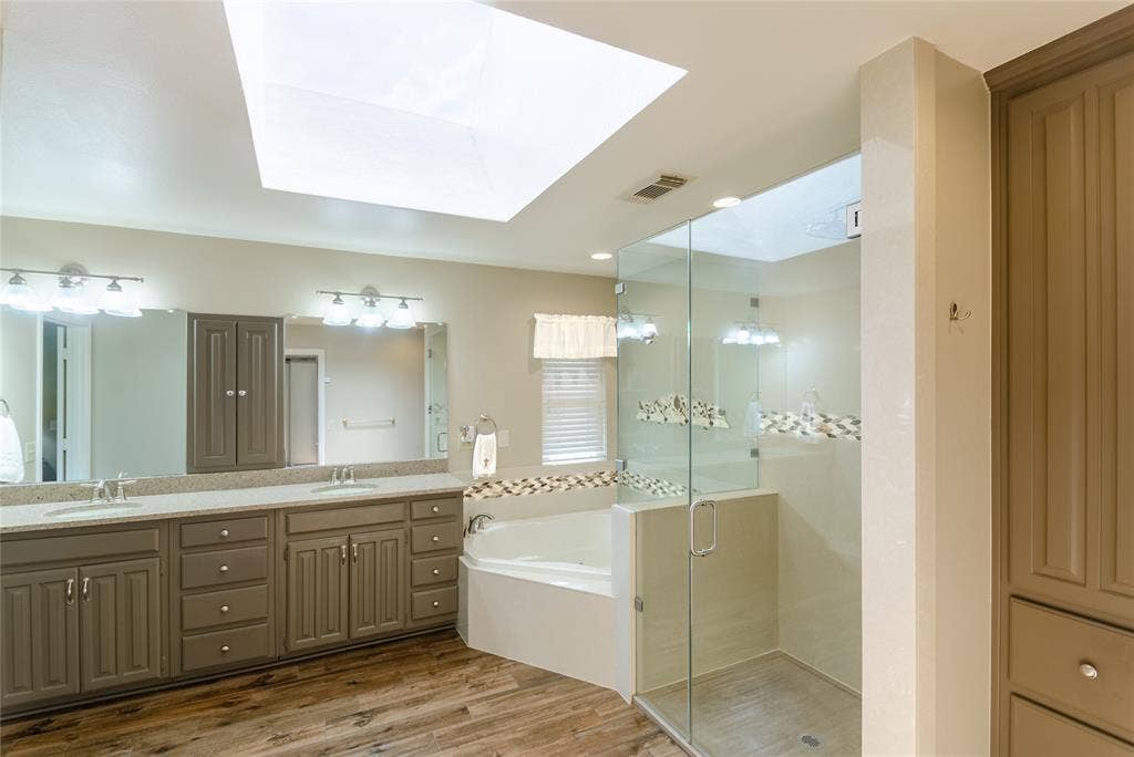 4009 Wilshire Court, Plano, TX 75023 Spacious bathroom featuring a skylight, dual vanity with extensive cabinetry, a built-in bathtub, and a glass-enclosed shower