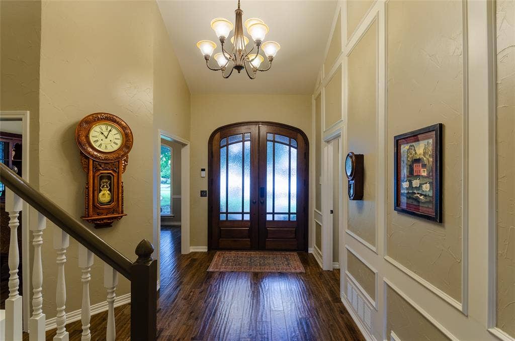 4009 Wilshire Court, Plano, TX 75023 Arched double entry doors with privacy glass, wood-finish flooring, staircase with white balusters, decorative wainscoting, and an overhead chandelier