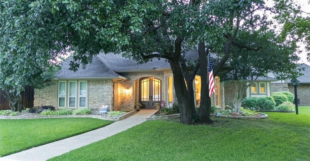 4009 Wilshire Court, Plano, TX 75023 Brick facade exterior with arched double entry doors, bay windows, mature trees, and a concrete pathway