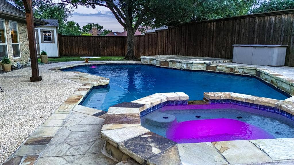 4009 Wilshire Court, Plano, TX 75023 Resort-style backyard featuring a geometric pool, integrated spa with stone coping, and expansive aggregate and flagstone patio