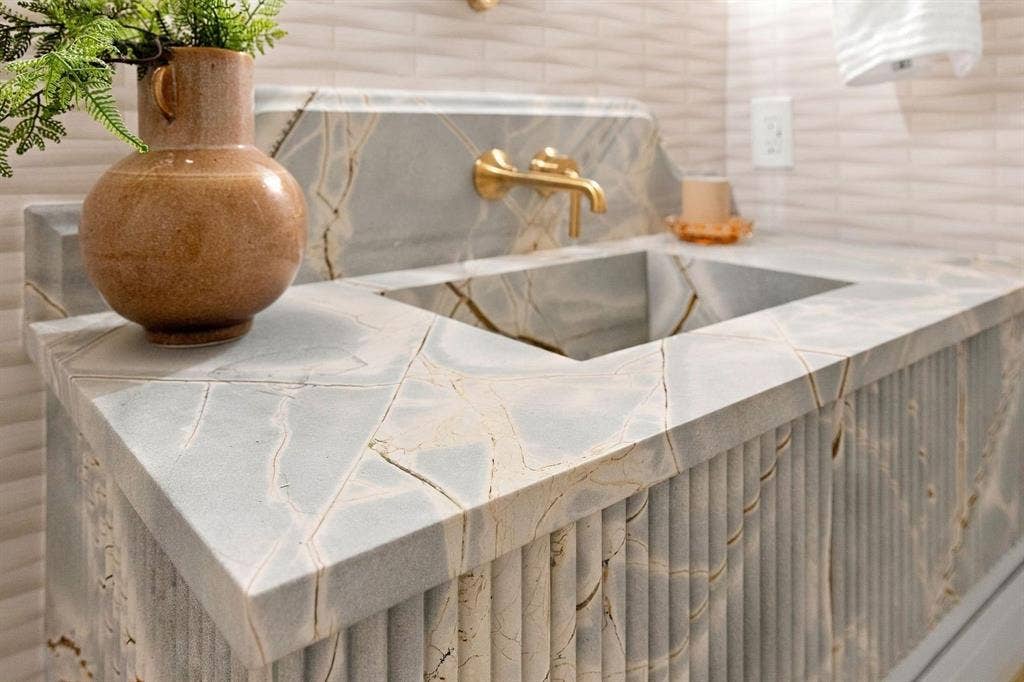 3368 Dorado Beach Drive, Farmers Branch, TX 75234 Integrated sink with a fluted vanity base, veined stone countertop, and brass wall-mounted faucet