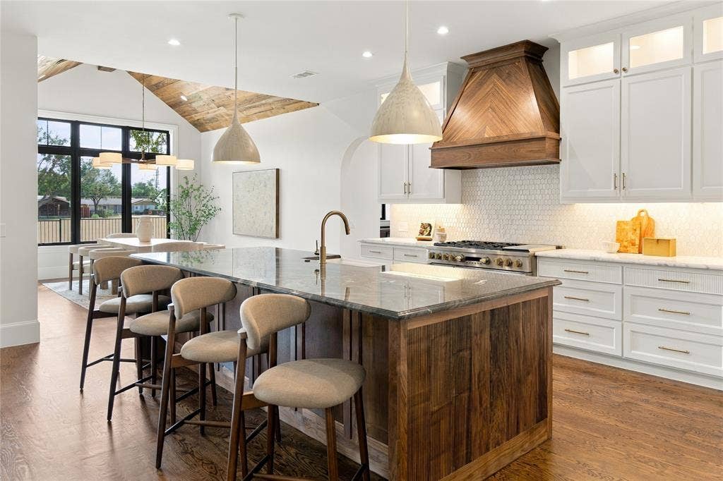 3368 Dorado Beach Drive, Farmers Branch, TX 75234 Spacious kitchen featuring a large island with a stone countertop, white cabinetry with gold-tone hardware, a wood-finish range hood, and wood-finish flooring