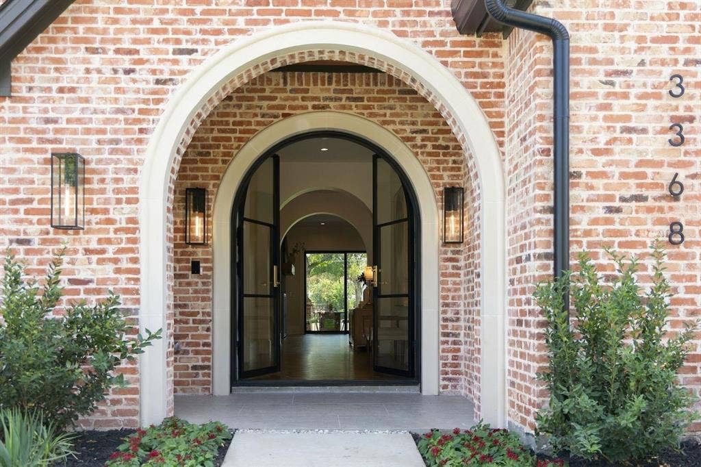 3368 Dorado Beach Drive, Farmers Branch, TX 75234 Red brick exterior with a white arched entry, featuring black-framed glass double doors and two exterior wall sconces