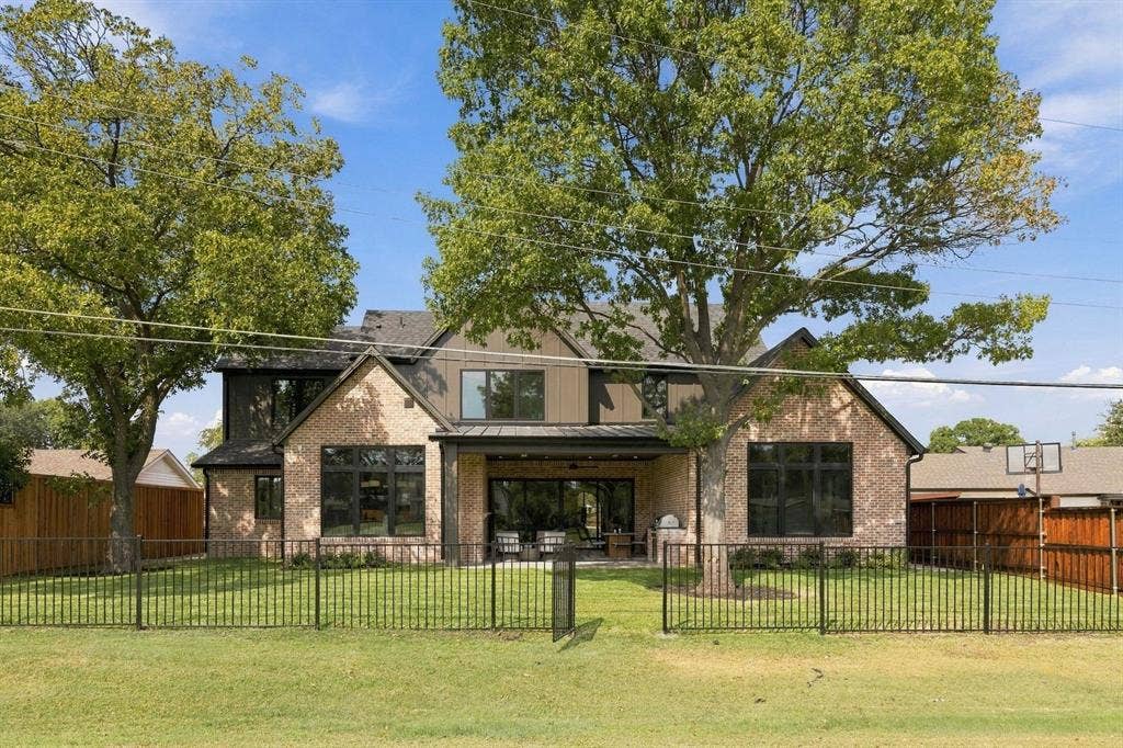 3368 Dorado Beach Drive, Farmers Branch, TX 75234 Brick and siding exterior with a covered patio, expansive lawn, mature trees, and black metal fencing