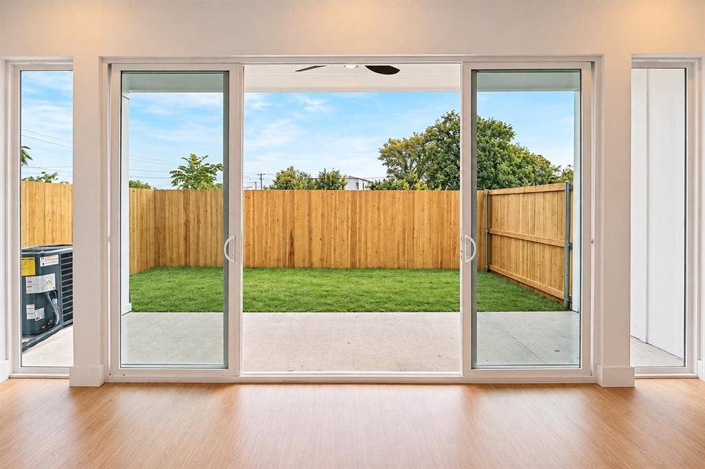 316 Avenue L, Dallas, TX 75203 Expansive sliding glass doors opening to a private backyard with a manicured lawn, concrete patio, and wood privacy fencing