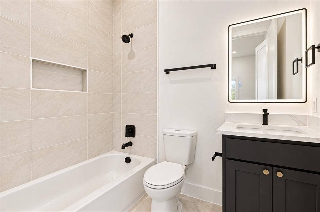 314 & 316 Avenue L, Dallas, TX 75203 Bathroom featuring a tiled shower surround with a built-in niche, white bathtub, black vanity with a white countertop, and an illuminated mirror