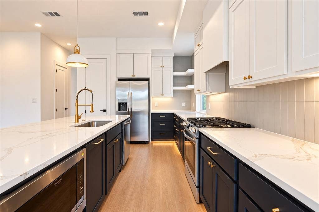 314 & 316 Avenue L, Dallas, TX 75203 Kitchen featuring a dual-tone cabinetry scheme, stainless steel appliances, white countertops with veining, wood-finish flooring, and a subway tile backsplash