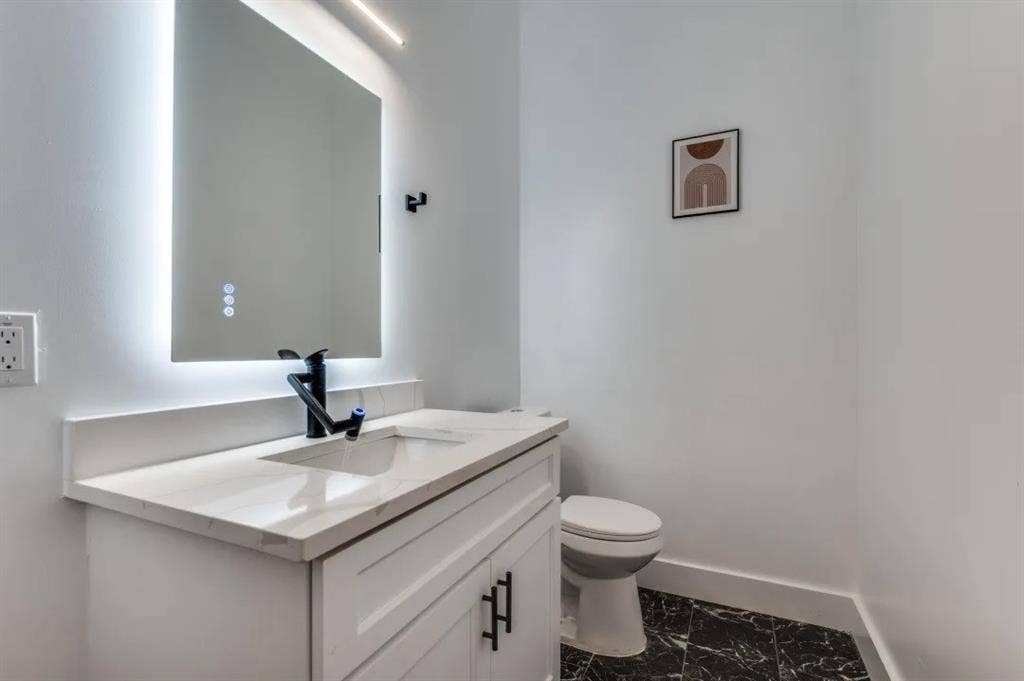 2802 Guymon Street, Dallas, TX 75212 White vanity with integrated sink, white countertop, illuminated mirror, black faucet, and patterned dark flooring