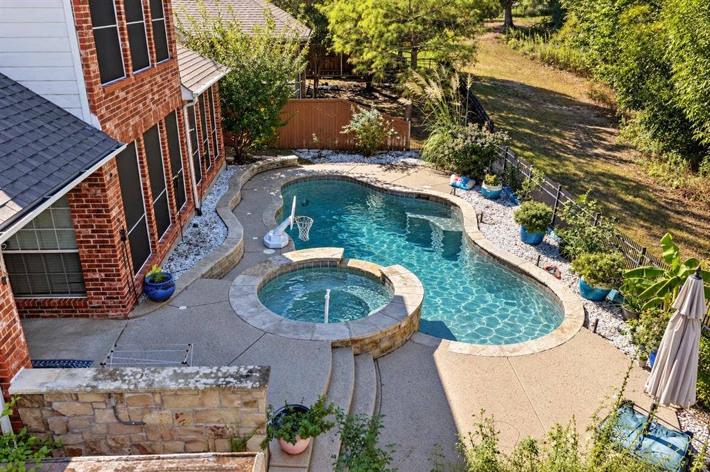 1905 Canyon Wren Drive, McKinney, TX 75071 Private backyard retreat with greenbelt views, a pool and raised spa, expansive concrete decking, and mature landscaping. Photo taken right after a few days of heavy thunderstorms and rain while the pool was undergoing maintenance. Water shown in the pool and spa has been digitally added.