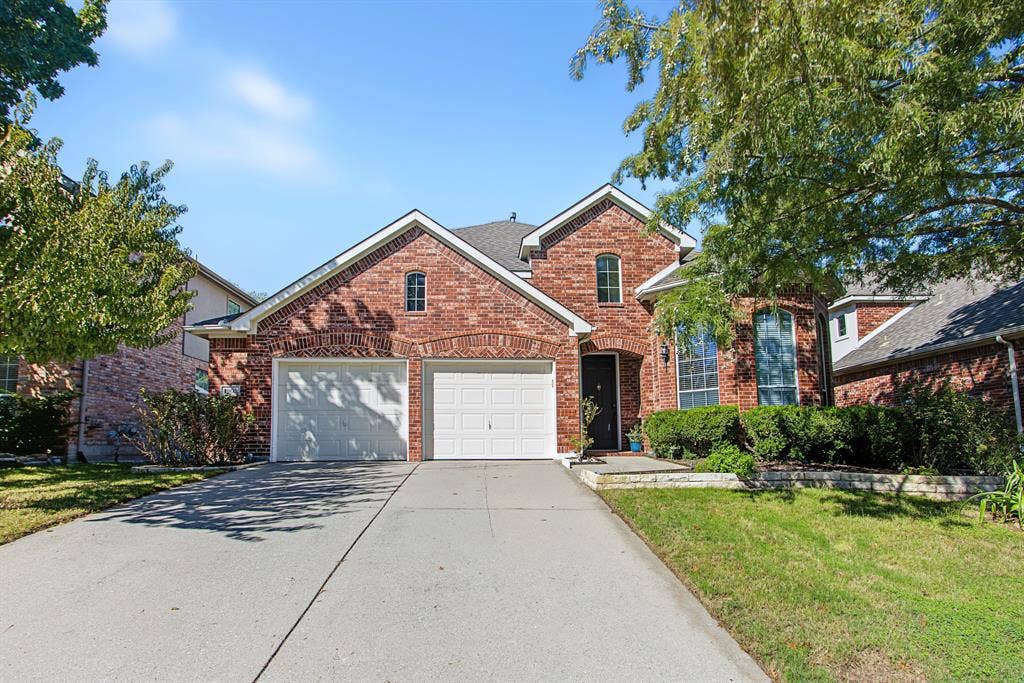 1905 Canyon Wren Drive, McKinney, TX 75071 Red brick exterior with garage doors, shingled roof, mature landscaping, and a concrete driveway