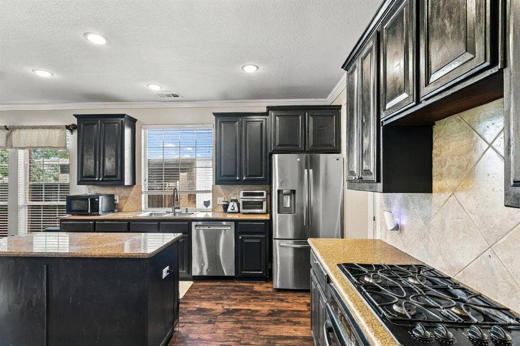 1905 Canyon Wren Drive, McKinney, TX 75071 Kitchen featuring dark wood-finish cabinetry, stainless steel appliances, a center island with a stone-finish countertop, and a gas cooktop