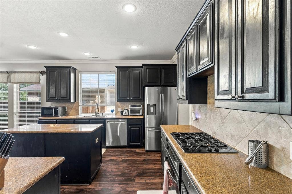 1905 Canyon Wren Drive, McKinney, TX 75071 Kitchen featuring dark wood cabinetry, granite countertops, tile backsplash, wood-style flooring, and stainless steel appliances