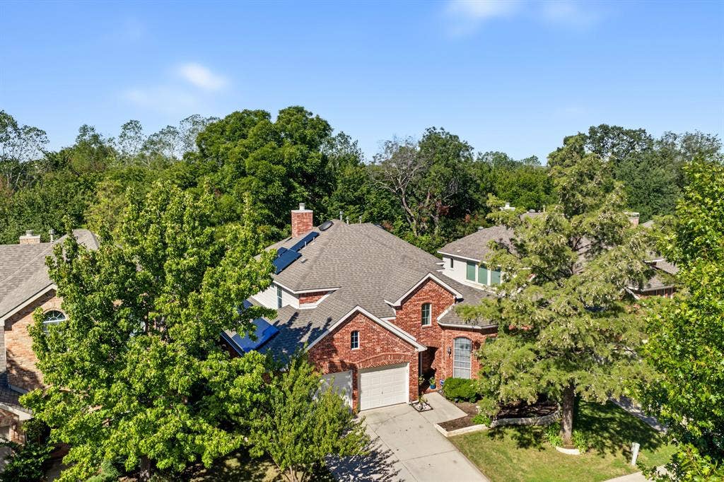 1905 Canyon Wren Drive, McKinney, TX 75071 Red brick exterior with garage doors, shingled roof, mature landscaping, and a concrete driveway