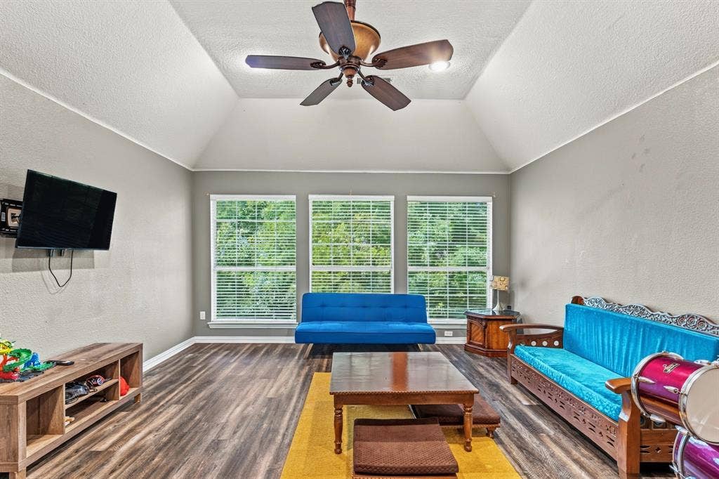 1905 Canyon Wren Drive, McKinney, TX 75071 Vaulted ceiling with a ceiling fan, three windows with blinds, wood-style flooring, and ceiling fan
