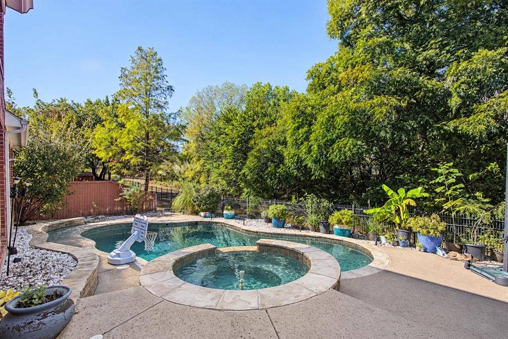 1905 Canyon Wren Drive, McKinney, TX 75071 Private backyard retreat with greenbelt views, a pool and raised spa, expansive concrete decking, and mature landscaping. Photo taken right after a few days of heavy thunderstorms and rain while the pool was undergoing maintenance. Water shown in the pool and spa has been digitally added.