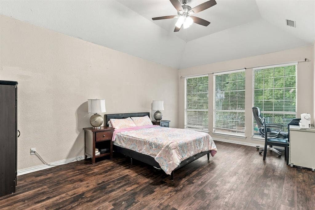 1905 Canyon Wren Drive, McKinney, TX 75071 Spacious primary bedroom showcasing wood-style flooring, abundant natural light from windows, vaulted ceiling, ceiling fan with integrated lighting
