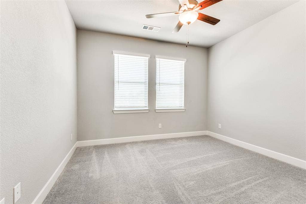 636 Courtyard Lane, Irving, TX 75039 Neutral wall paint, two windows with blinds, ceiling fan with integrated lighting, and gray carpet flooring